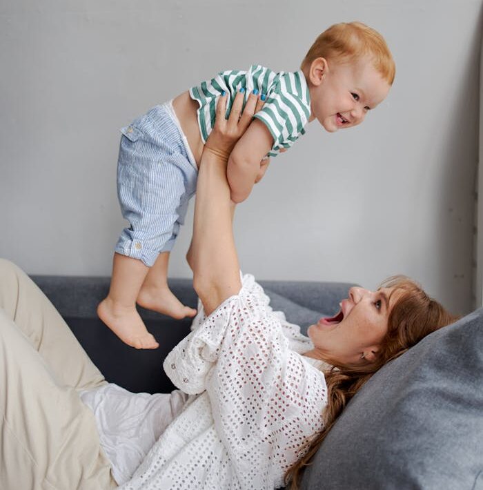 Mother playfully lifting her smiling baby indoors, showcasing love and happiness.
